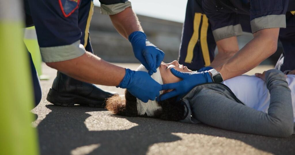 Injured woman receiving emergency treatment from two nurses, with her head wrapped for stabilization after a car accident, seeking help from personal injury lawyers.
